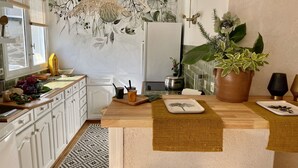 Una cucina moderna con mobili bianchi, un pannello decorativo dietro il piano cottura, un lampadario a sospensione e una grande pianta in vaso.
