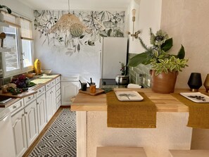 Een moderne keuken met witte kastjes, een decoratieve spatwand, een hanglamp en een grote potplant.