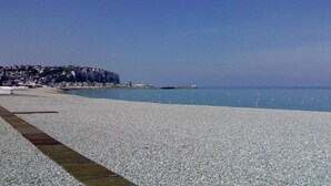 A pebble beach with a wooden walkway, a lighthouse, and buildings on a cliff in the background. - Townhouse near Bay of Somme and Norman Beaches (Rieux)