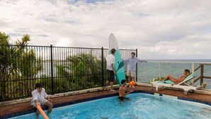 A swimming pool with people around it, a surfboard, and a view of the sea. - Magical Views of Dee Why (Dee Why)