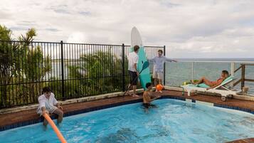 Une piscine entourée de personnes, une planche de surf et une vue sur la mer.