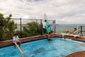 A swimming pool with people around it, a surfboard, and a view of the sea. - Magical Views of Dee Why (Dee Why)