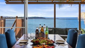 A dining table set with plates, cutlery, and a fruit basket, overlooking a body of water. - Magical Views of Dee Why (Dee Why)
