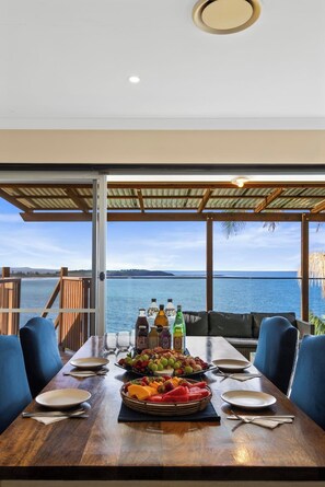 A dining table set with plates, cutlery, and a fruit basket, overlooking a body of water. - Magical Views of Dee Why (Dee Why)