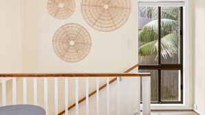 A staircase with a wooden handrail and white balusters, leading to a door with a view of palm trees outside. - MAGICAL VIEWS OF DEE WHY (Dee Why)