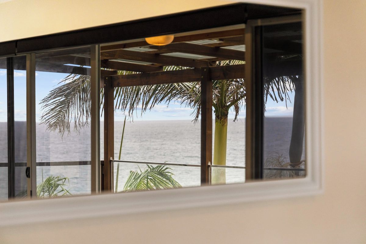 A room with a view of the ocean through a window with a wooden frame and a glass panel.