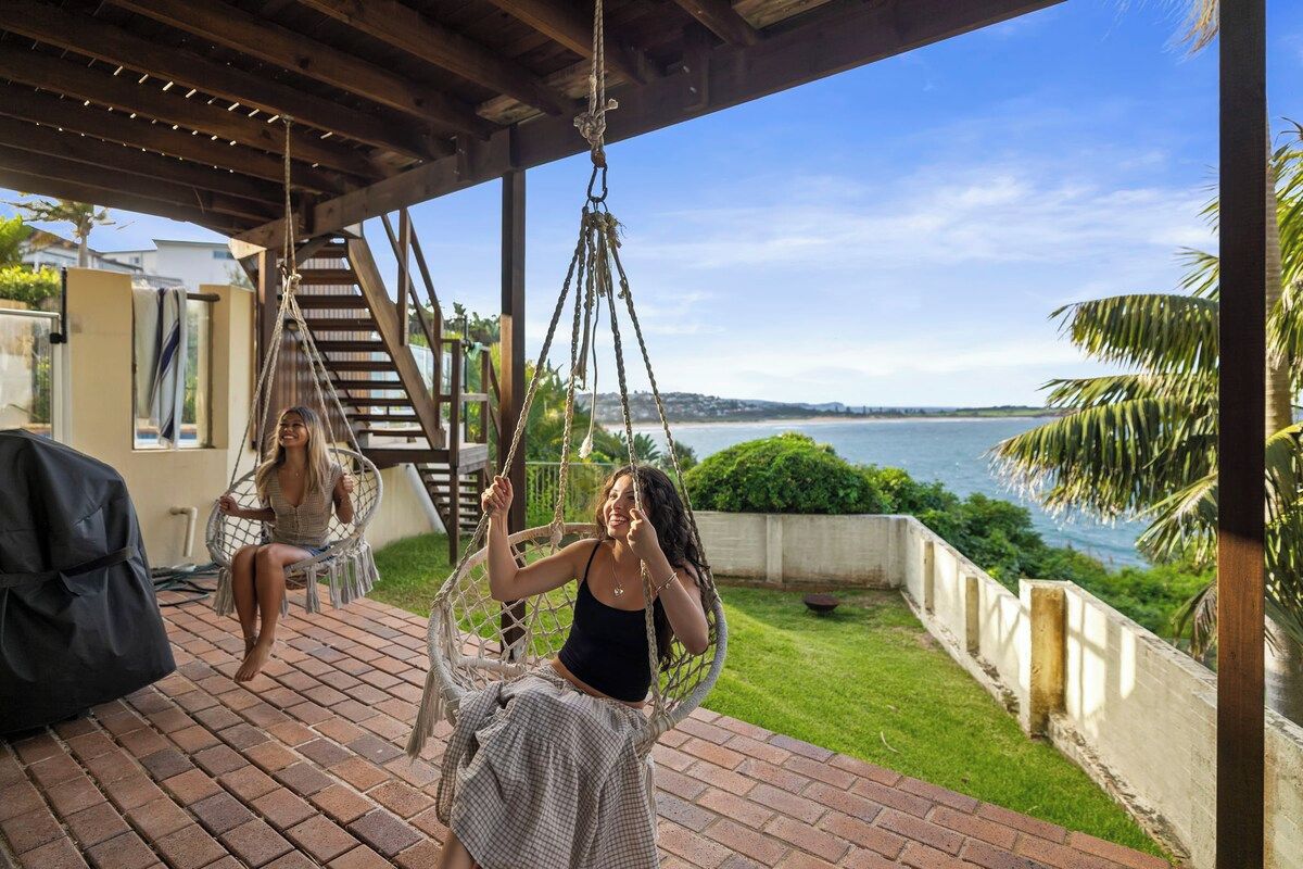 A covered outdoor area with a swing chair and a view of the sea.