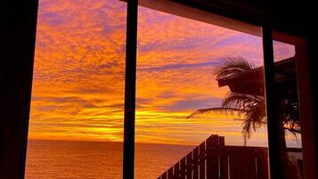 A sunset view through a window with a wooden railing and a palm tree.