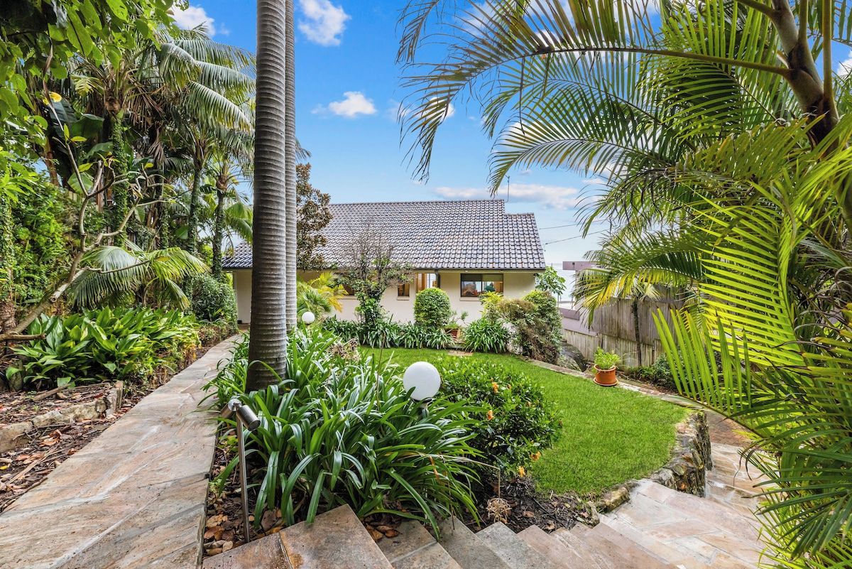 A house with a tiled roof, surrounded by a well-maintained garden with various plants and a stone pathway leading to the entrance.