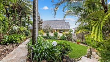 A house with a tiled roof, surrounded by a well-maintained garden with various plants and a stone pathway leading to the entrance.