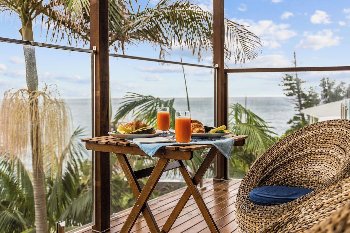 A wooden deck with a table set for breakfast, overlooking a tropical beach.
