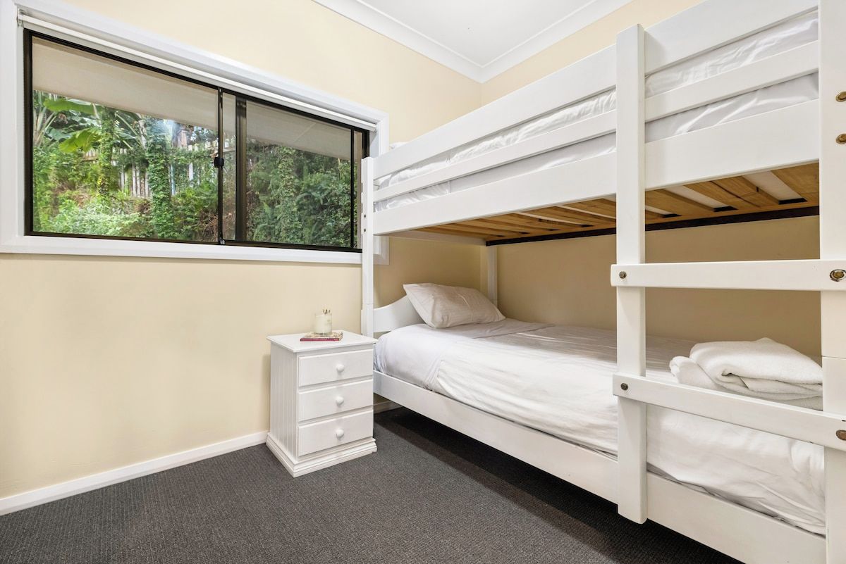 A bunk bed room with a window, a bedside table, and a carpeted floor.