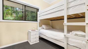 A bunk bed room with a window, a bedside table, and a carpeted floor.
