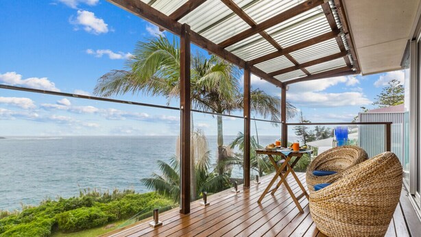 A wooden deck with a view of the ocean, a covered area with a table and chairs, and a large woven chair. - MAGICAL VIEWS OF DEE WHY (Dee Why)