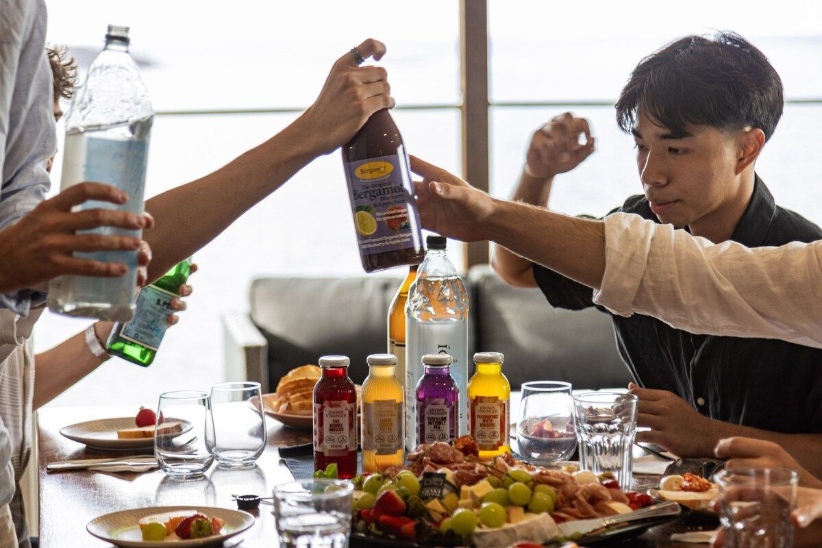 A group of people at a table with various food items and drinks, including bottles and glasses.
