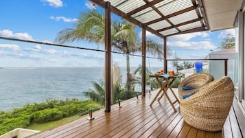 Une terrasse en bois offrant une vue sur l’océan, une table avec des chaises et un espace abrité avec un toit en métal.