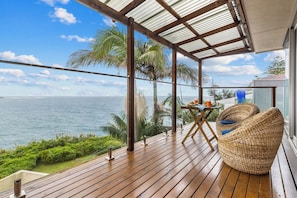 Une terrasse en bois offrant une vue sur l’océan, une table avec des chaises et un espace abrité avec un toit en métal.