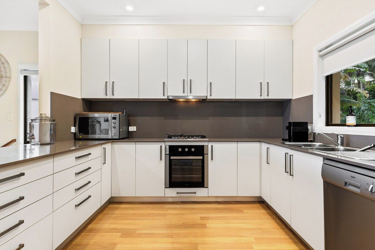 A modern kitchen with white cabinets, a built-in oven, a microwave, and a dishwasher.