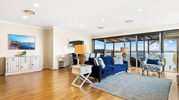A spacious living room with a blue sofa, a white cabinet, and a large window offering a view of the sea.