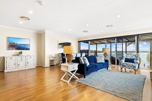 A spacious living room with a blue sofa, a white cabinet, and a large window offering a view of the sea.