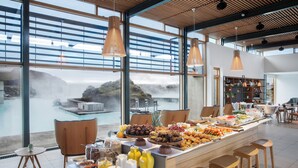 Ein reichhaltiges Buffet mit verschiedenen Speisen und Blick auf ein Gewässer durch große Fenster.