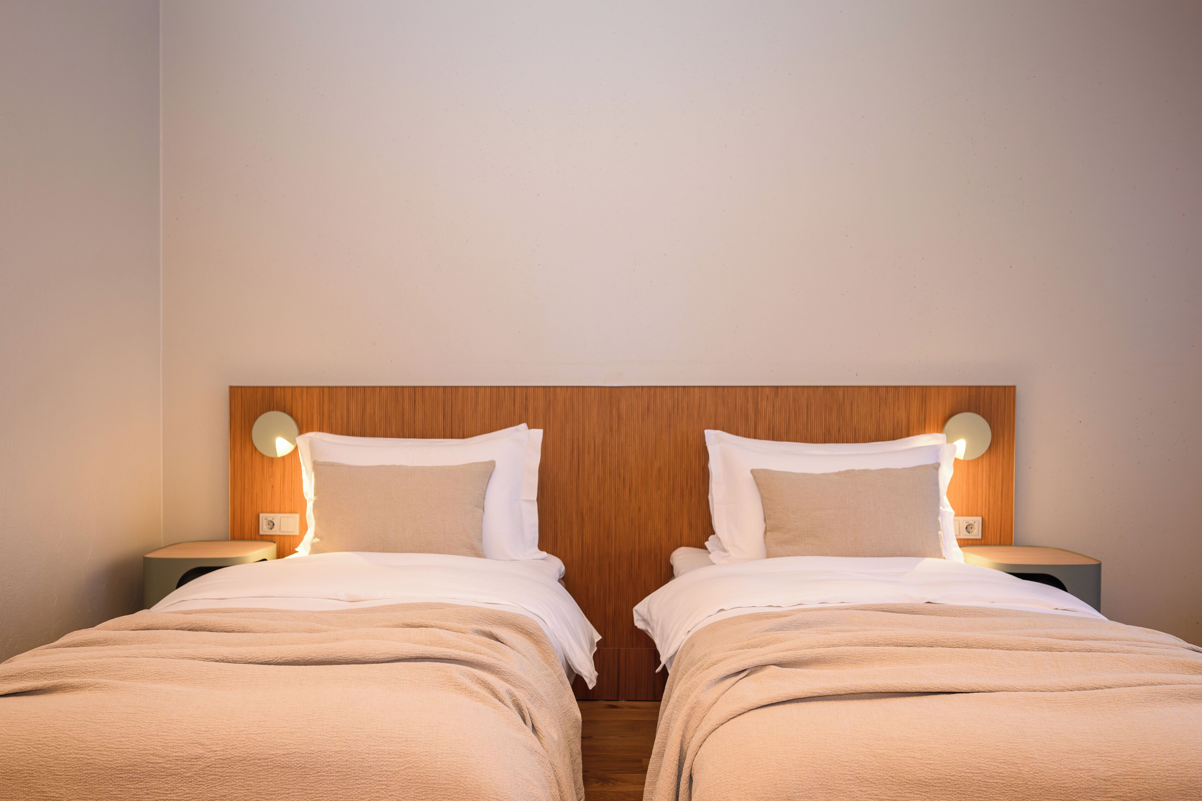 A double room with two beds, wooden headboard, bedside lamps, and a neutral color scheme.