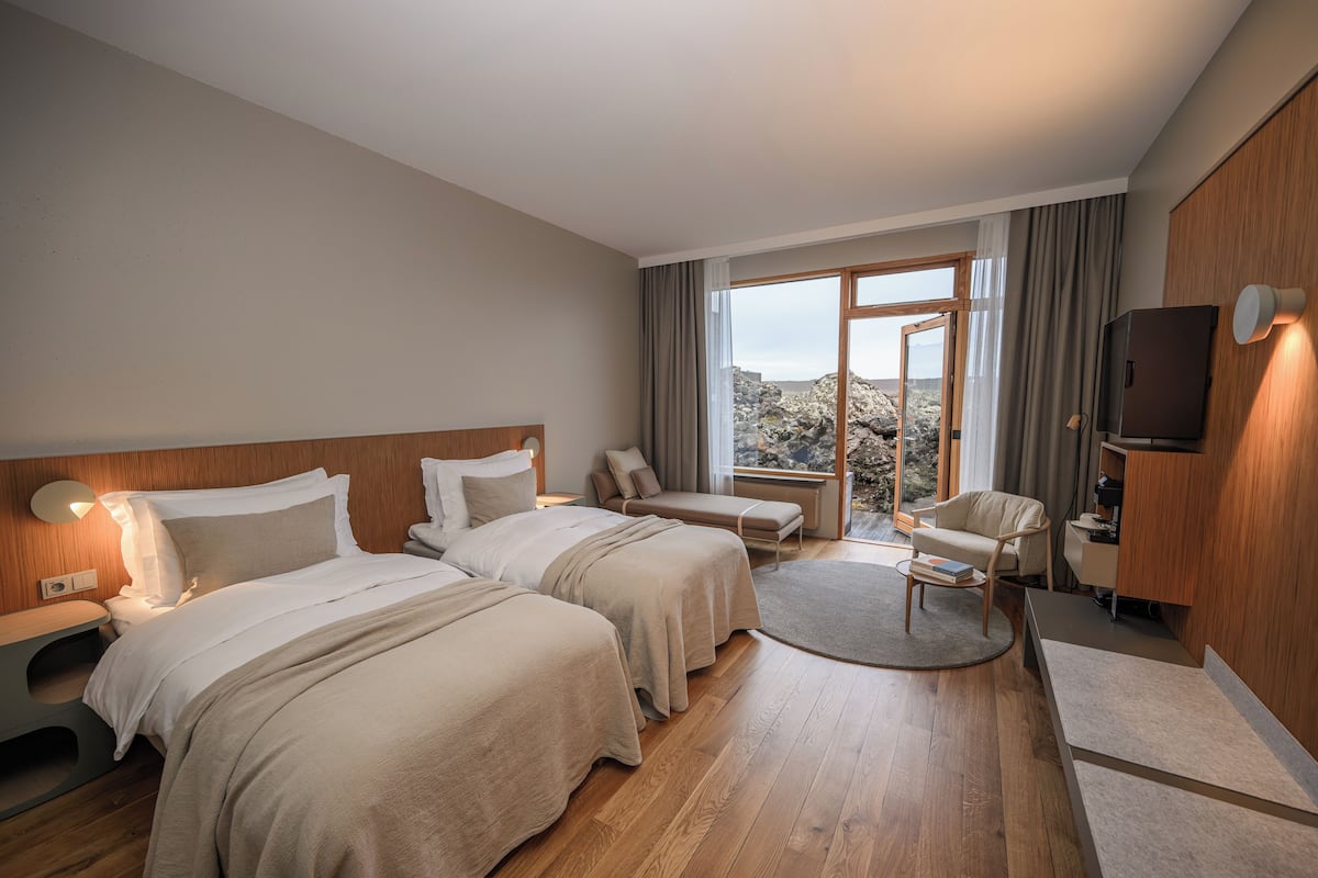 A hotel room with two beds, a sitting area, a TV, and a view of the outdoors.