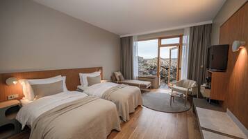 A hotel room with two beds, a sitting area, a TV, and a view of the outdoors.