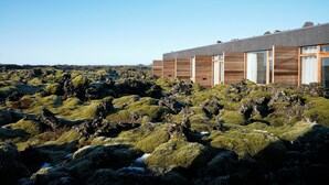 Ein modernes Gebäude mit großen Fenstern und einer Holzfassade, gelegen auf felsigem Gelände mit moosbewachsenen Steinen.