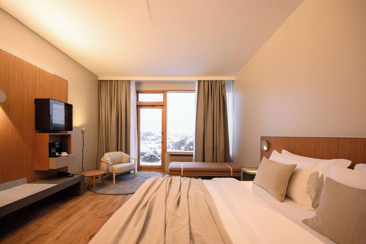 A hotel room with a bed, a TV, a chair, a desk, and a window with curtains.