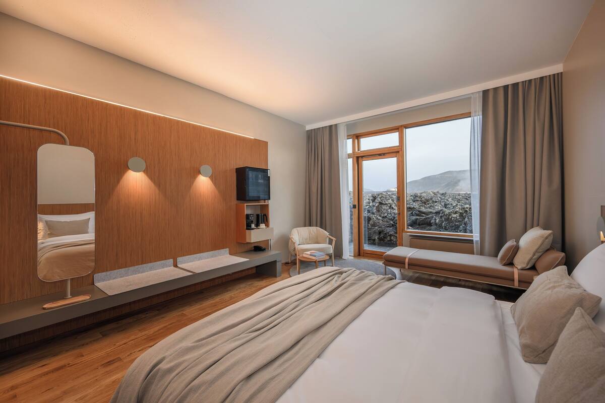 A modern hotel room with a large bed, a seating area with a view, a TV, and a wooden panel wall.