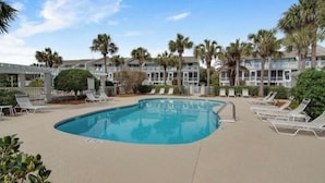 A swimming pool with lounge chairs, palm trees, and a building with balconies in the background. - Beach Club Villa 29 by Deserving Vacations (Isle of Palms)