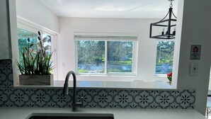 A kitchen with a white countertop, a sink, and a window with a view of greenery.