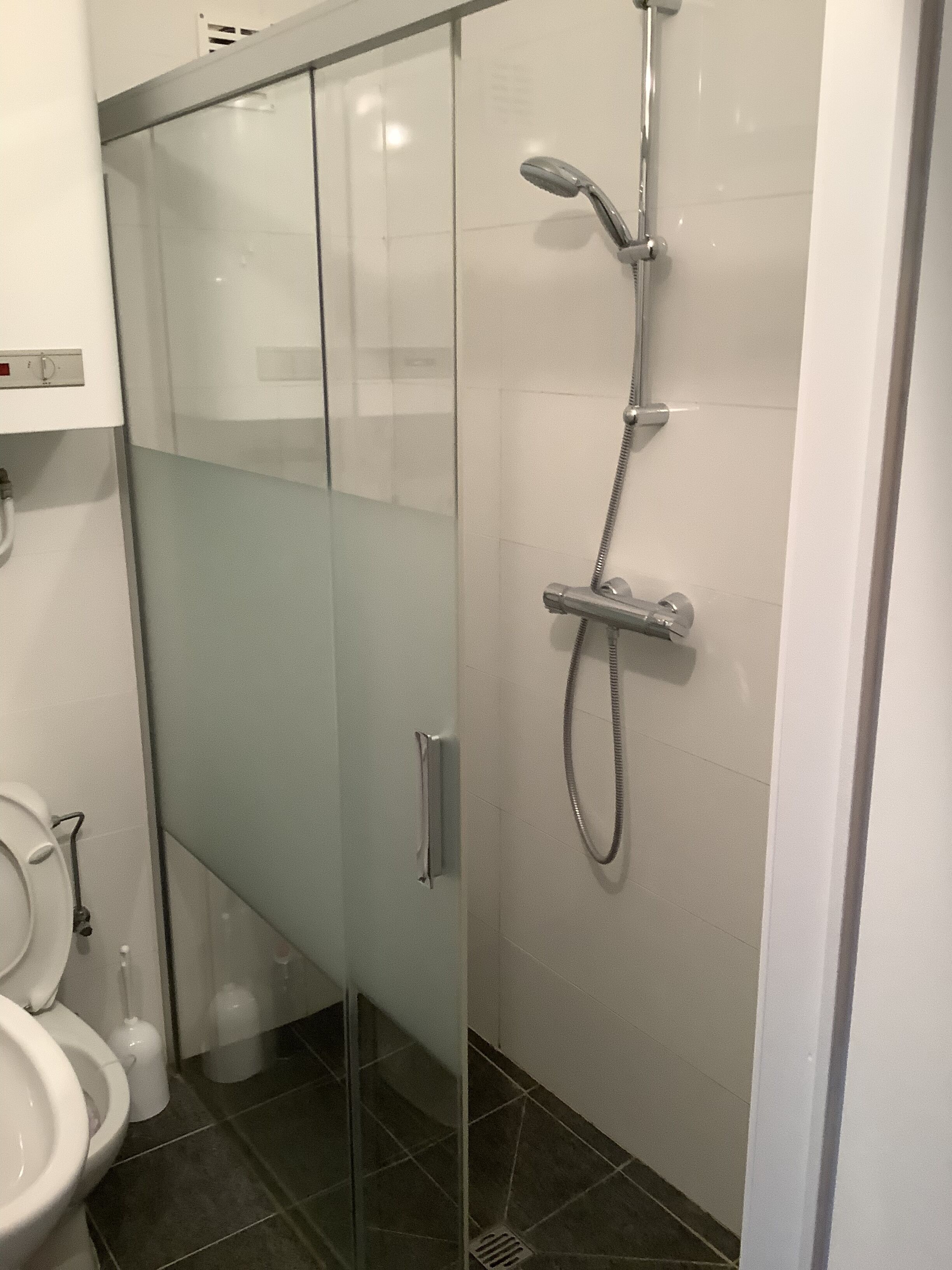 Un baño moderno con ducha separada por mampara de vidrio, inodoro y lavamanos.
