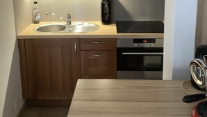 A compact kitchen with wooden cabinets, a stainless steel sink, a coffee maker, and a built-in oven. - Sun-oriented studio Sint-Idesbald with beautiful sea view (Koksijde)