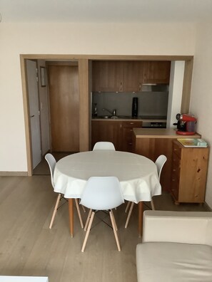 Eine kleine Küche mit Holzausstattung, einer Kaffeemaschine und einem Essbereich mit rundem Tisch und weißen Stühlen.