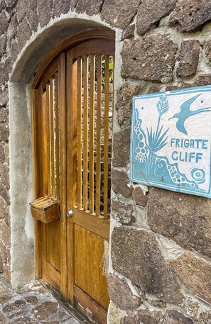 Uma porta de madeira com ripas verticais, uma parede de pedra e uma placa com a inscrição "FRIGATE CLIFF".