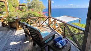 A wooden deck with a bench and a table, overlooking a pool and the ocean.