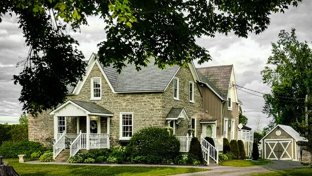 Une grande maison en pierre avec un porche à l’avant, un garage et une pelouse bien entretenue.