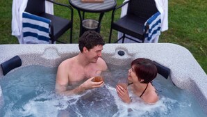 Un bain à remous pour deux personnes, une table avec un plateau de nourriture et deux chaises avec des serviettes.