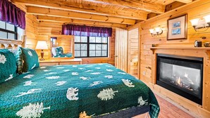 A cozy log cabin bedroom with a large bed, a fireplace, and a window with a view. - Charming & Quiet Mtn-Top Cabin w Grand Panoramic Mountain Views!! DOG Friendly! (Sevierville)
