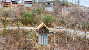 A cabin-style building with a wooden exterior and a pitched roof, surrounded by a forested area with a dirt path leading to it. - Charming & Quiet Mtn-Top Cabin w Grand Panoramic Mountain Views!! DOG Friendly! (Sevierville)