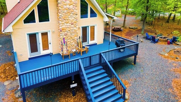A two-story house with a stone chimney, a blue deck, and a staircase leading to the entrance. - 4BDRM Games Family Friendly Fire Pit Masthope (Lackawaxen)