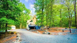 A rustic cabin with a stone exterior, a wooden deck, and a gravel driveway surrounded by trees. - 4BDRM Games Family Friendly Fire Pit Masthope (Lackawaxen)