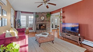 A living room with a fireplace, a ceiling fan, a large TV, and a red wall. - Quiet 6BR Family Getaway Near Beach + Casinos (Atlantic City)