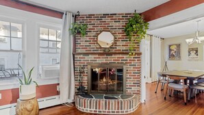A room with a brick fireplace, wooden flooring, a dining table with chairs, and a large window with curtains. - Quiet 6BR Family Getaway Near Beach + Casinos (Atlantic City)