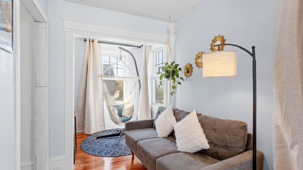 A living room with a grey sofa, a hanging chair, a floor lamp, and a view of the outdoors through a window. - Quiet 6BR Family Getaway Near Beach + Casinos (Atlantic City)