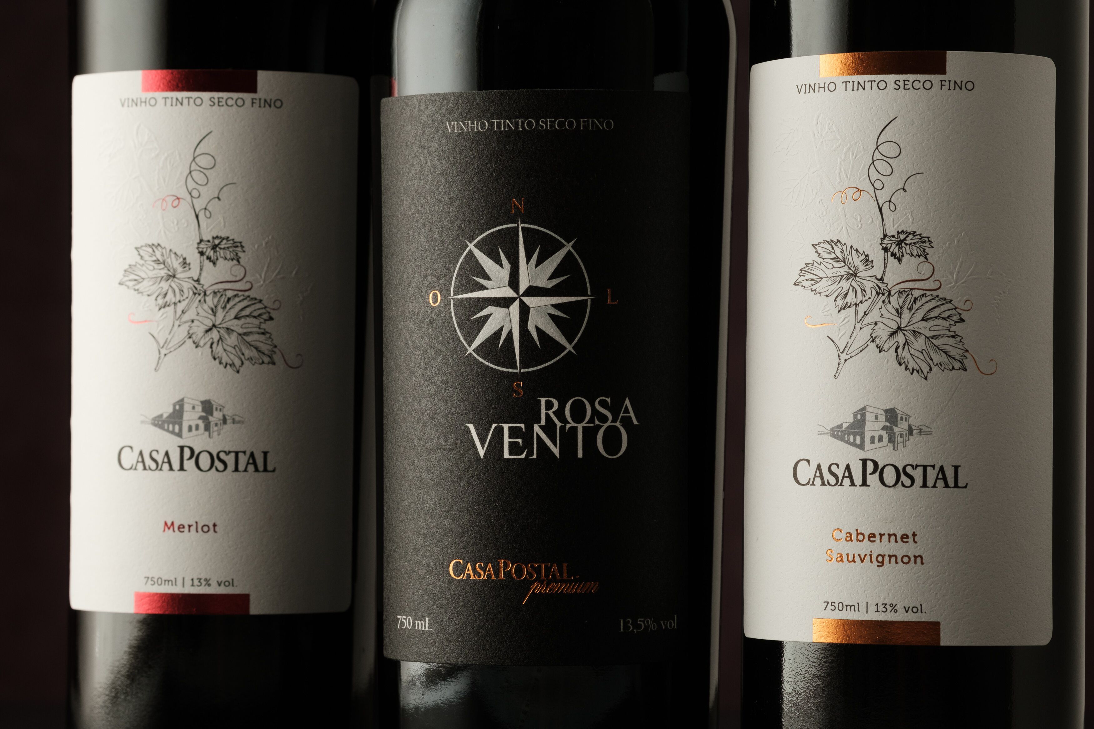 Three wine bottles labeled 'CasaPostal' with different types of wine: Merlot, Rosa Vento, and Cabernet Sauvignon. Each bottle has a unique design and label.