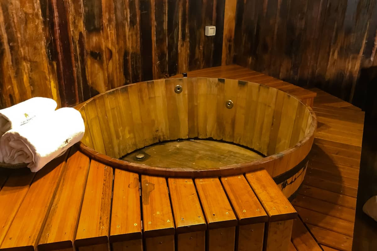 A wooden hot tub with a white towel on a wooden bench.