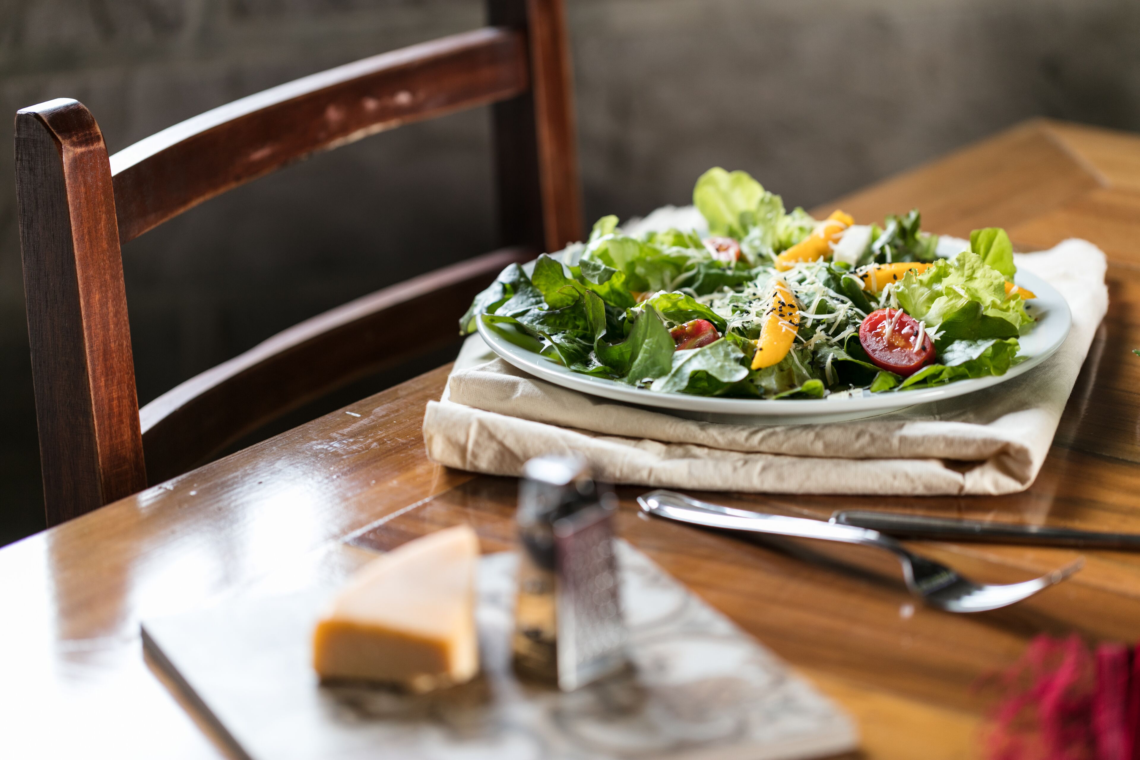Une table en bois sur laquelle se trouvent une assiette de salade, un morceau de fromage et un couteau.